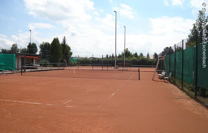 Ein roter Tennisplatz umrahmt von grünen Bäumen.