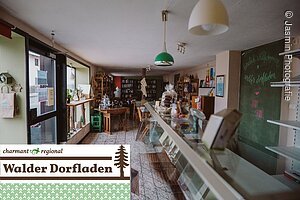 Der Dorfladen in Wlad. Rechts eine Theke. Links der Eingang und im Hintergrund die Ware des Dorfladens. In der linken unteren Ecke steht: charmant regional Walder Dorfladen
