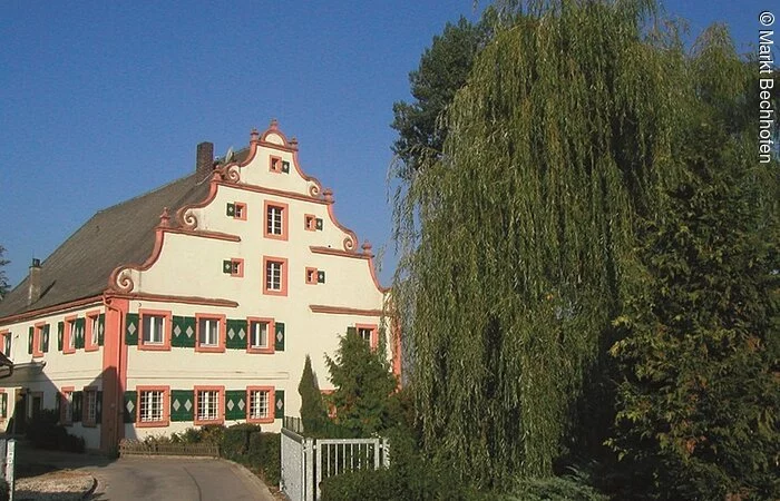 Eine barockes Gebäude mit vier Ebenen. Das Haus mit weißer Fassade und grünen Fensterläden in den ersten zwei Ebenen.