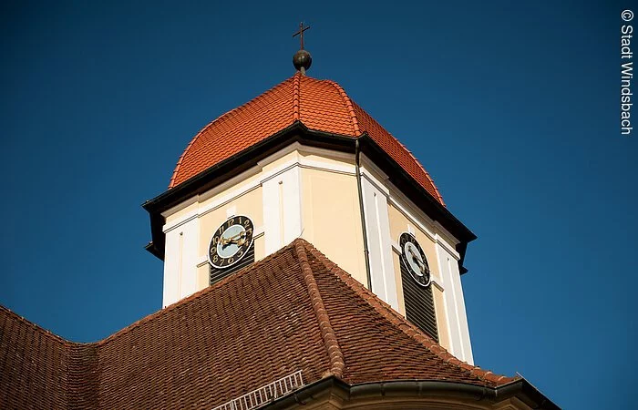 Blick von unten auf eine Kirchturmspitze. Ein Turm mit weiß-gelber Fassade und rotem Haubendach.