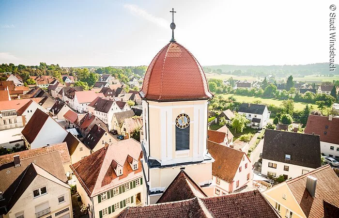 Blick von oben auf den Kirchturm der Stadtkirche Windsbach. Ein Turm mit weißer Fassade und rotem Haubendach.
