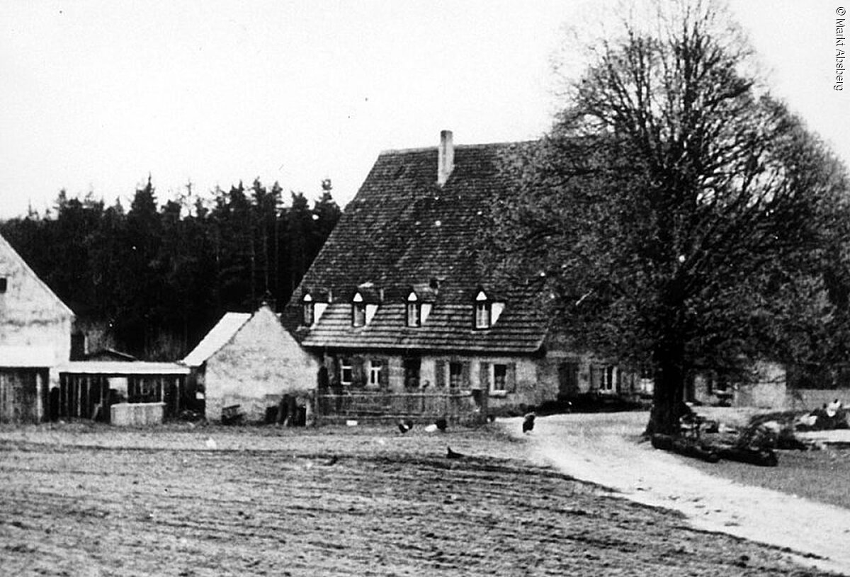 Schwarz-weiß Foto eines alten Hauses. Direkt vor dem Haus ein Baum. Ein Weg führt am Haus vorbei.