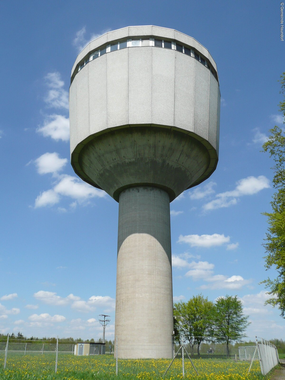 Ein Wasserturm aus Beton ragt in den blauen Himmel. Auf einem dünneren Zylinder sitzt ein breiterer Zylinder.