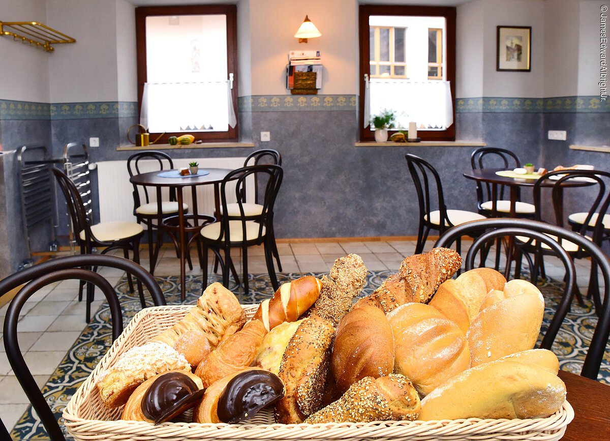 Im Vordergrung ein Korb mit Semmeln und Gebäck. Im Hintergund die Tische und Stühle des Stadtcafé Merkendorf. Die Wände sind weiß gestrichen und blau gefließt.