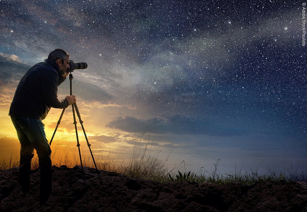 Ein Mann macht Fotos des funkelnen Sternenhimmels bei Sonnenuntergang.
