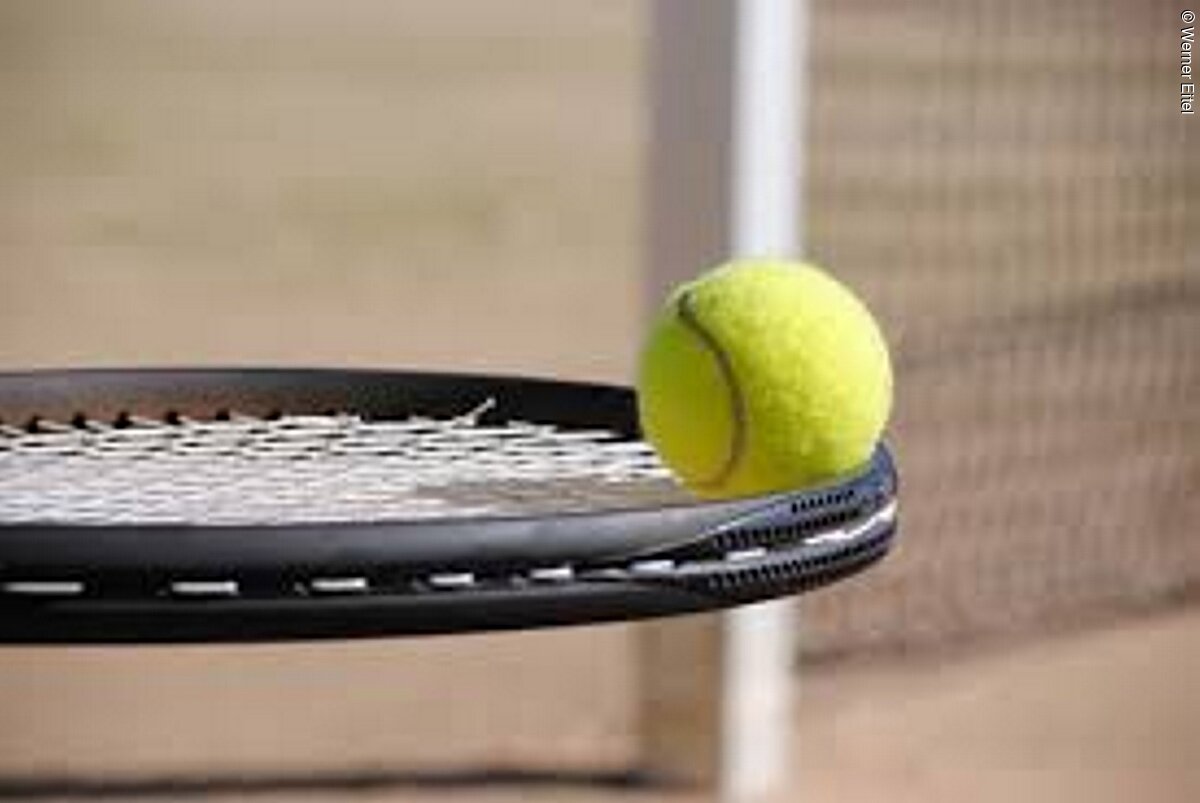 Nahaufnahme eines Tennisschlägers. Spitze eines Tennisschlägers auf welcher ein gelber Tennisball liegt.