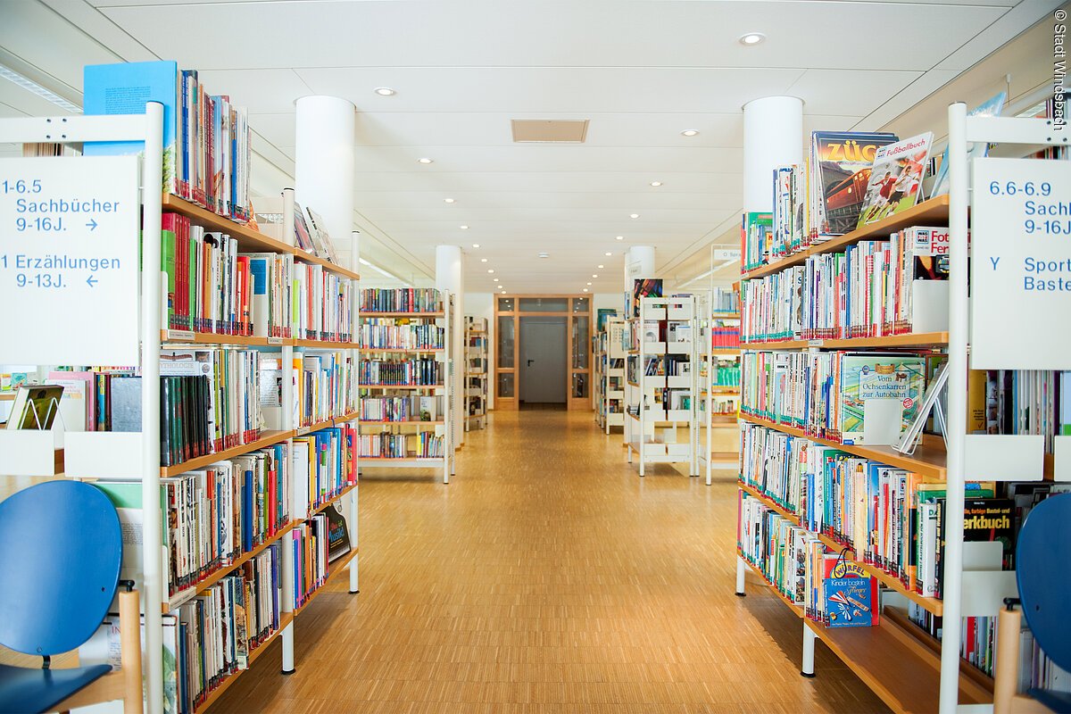 In einem weißen Raum mit Holzparkett stehen Regale mit Büchern.