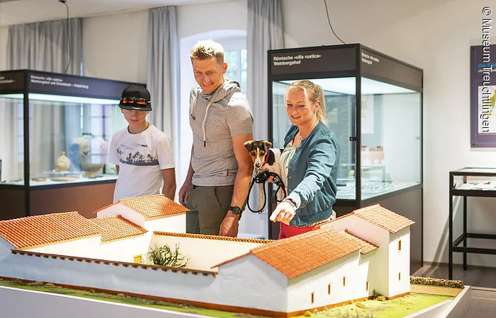 Eine Familie besucht die Abteilung der Abteilung Vor- und Frühgeschichte im Museum. Sie Blicken auf eine Nachbildung einer sogenannten Villa Rustica.