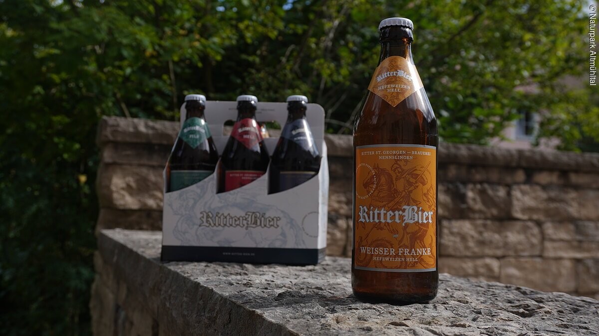 Bier Ritter St. Georgenbräu Eine Flasche Ritterbier und ein Sechserpack stehen auf einer Steinmauer im Freien.