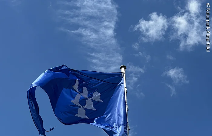 Vor einem blauen Himmel mit wenigen Wolken ist die blaue Flagge der Burg Pappenheim zu sehen.