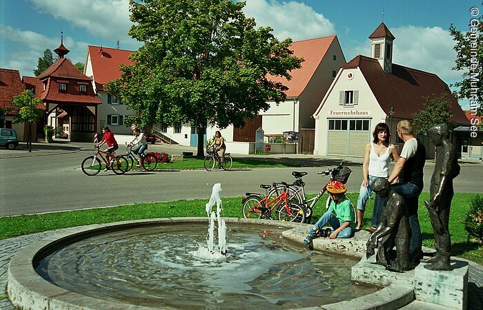 Radler legen eine kleine Rast am Brunnen in der Ortsmitte von Muhr am Altmühlsee ein.