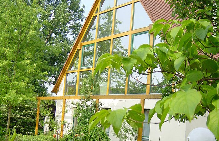 Verspiegelte Rückansicht Auch die Scheiben auf der Hinterseite des Kunstateliers "Zimmermann" in Arberg sind verspiegelt. Im Vordergrund blühende Blumen.