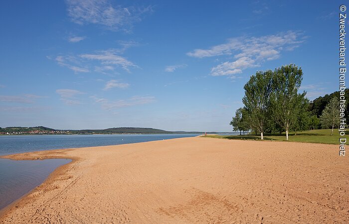 Bild von Liegewiese, Sandstrand und tiefblauem Großen Brombachsee beim Seezentrum Allmannsdorf Breiter, flacher Sandstrand in Allmannsdorf am großen Brombachsee. Im Hntergund beginnt links der Brombachsee und rechts eine Liegewiese mit Bäumen.
