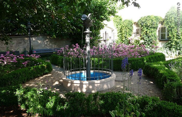 Der kleine Brunnen umrahmt von Blumenbeeten.