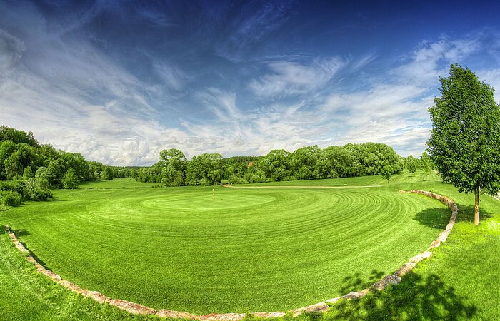 Grün der Bahn 18 Große grüne Wiese eines Golfplatzes. Der PLatz ist umgebennvon Bäumen und Sträuchern.