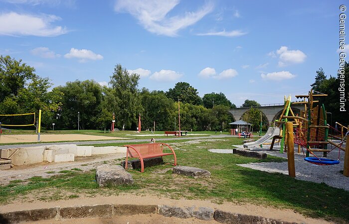 Ein großer Spielplatz mit Klettergerüst, Rutsche, Sandkasten und Beachvolleyballfeld.