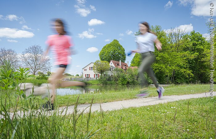 Zwei Mädchen rennen auf dem Weg neben dem Karlsgraben hintereinander. Die Mädchen sind leicht verschwommen.