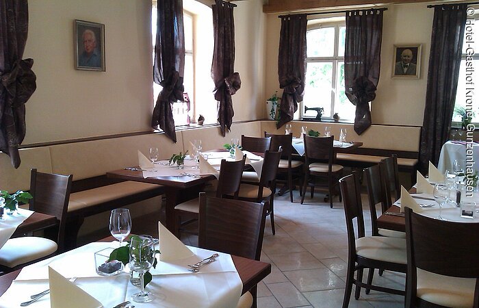 Hotel-Gasthof Krone Blick in einen Gastraum mit beigen Wänden und braunen Vorhängen. Entlang der Wände Bänke. Davor Tische und Stühle aus dunkelbraunem Holz. Die Tische sind festlich mit weißen Tischdecken und Servietten gedeckt.