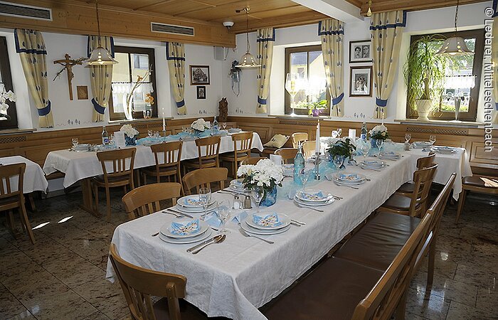 Ein gedeckter Tisch im Saal vom Gasthof Lederer. In zwei Reihen bestuhlte Tische mit Stühlen. Darauf weiße Tischdecken und Gedeck.