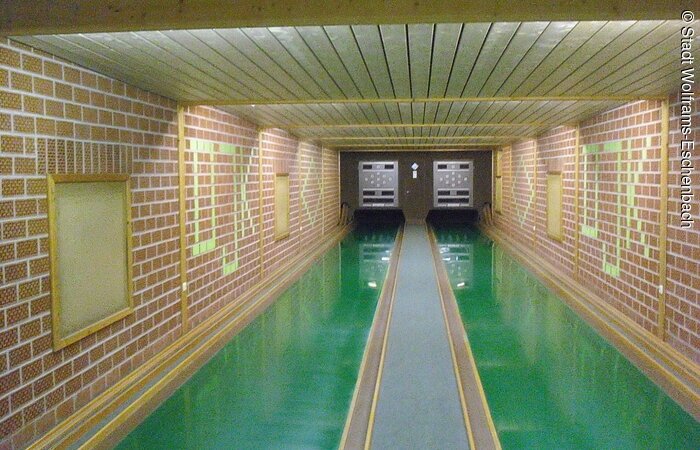 Zwei grüne Kegelbahnen umgeben von langen gemauerten Wänden.