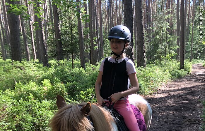 Ein junges Mädchen reitet auf einem Pony durch den Wald.
