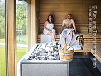 Paar sitzt in der Sauna und im Vordergrund steht der Aufgusseimer auf dem Ofen Paar sitzt in der Sauna und im Vordergrund steht der Aufgusseimer auf dem Ofen