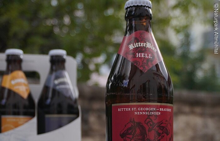 Bier Ritter St. Georgenbräu Zwei Bierflaschen mit Etiketten "RitterBier" vor einer Steinwand. Eine Flasche hat ein rotes, die andere ein blaues Etikett.
