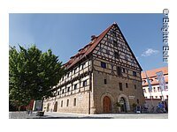 Ein großes Fachwerkhaus mit 6 Ebenen. Die Fassade der unteren zwei Stöcke besteht aus Stein, darüber braunes Fachwerk mit weißer Fassade.