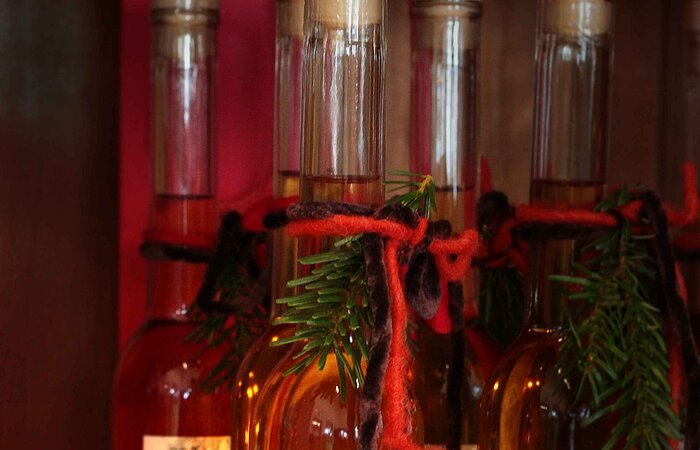 5 Glasflaschen Winterlikör, die mit kleinem Fichtenzweig und roter Schleife geschmückt sind, um das Arrangement ist eine LED-Lichterkette drapiert