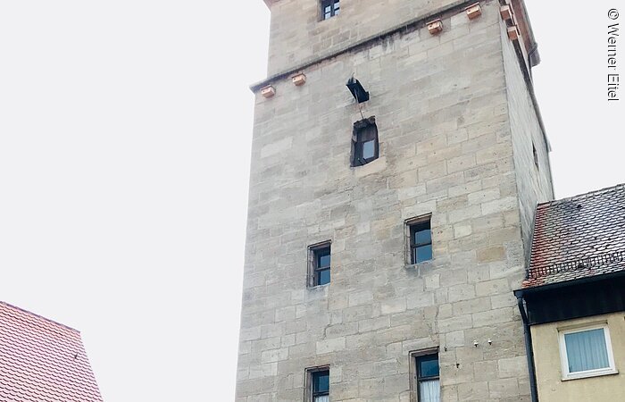 Ein hoher Stadtturm aus Stein. Durch den Turm führt ein Stadttor.