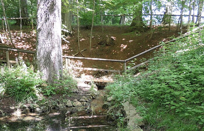 In einer Senke befindet sich ein von Steinen und Holzzäunen begrenzter kleiner Weiher.