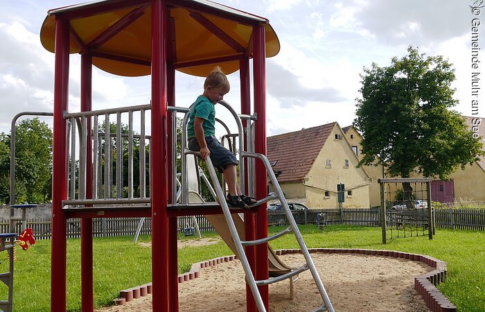 Spielplatz in Muhr am See - Kirche St. Jakobus Roter, 6-eckiger Turm - ein Junge möchte gerade auf die Leiter steigen.