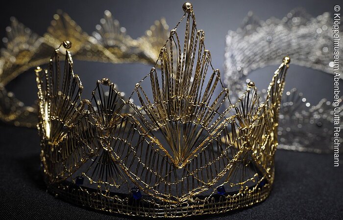 Eine geklöppelte goldenen Krone liegt auf einem grauen Untergrund.