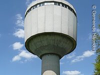 Ein Wasserturm aus Beton ragt in den blauen Himmel. Auf einem dünneren Zylinder sitzt ein breiterer Zylinder.