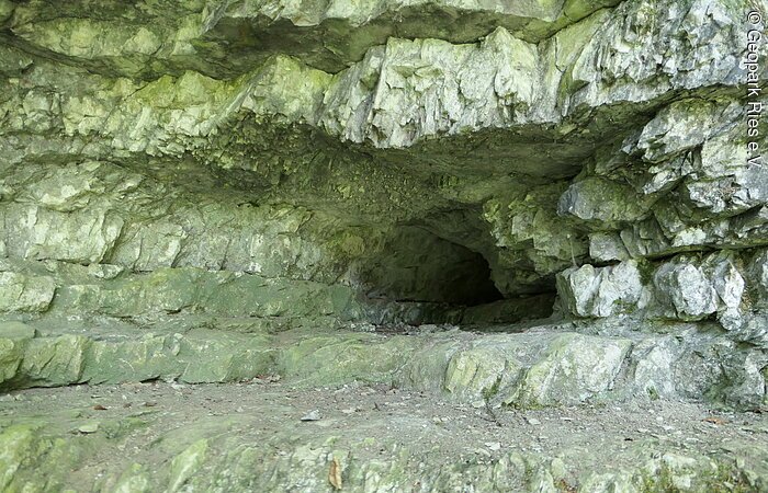 In einer Felswand aus geschichtetem Gestein befindet sich ein Loch.