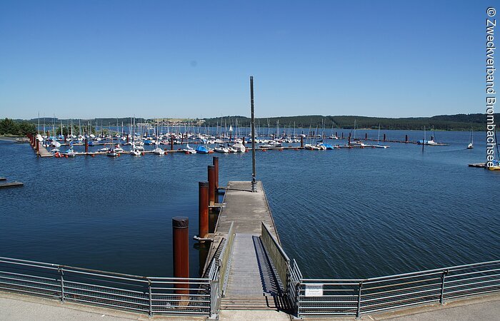 Seezentrum Ramsberg Der Seglhafen am Brombachsee. Ins Wasser führt ein schmaler Steg. Dahinter liegt etwas entfernt der Segelhafen mit vielen Segelbooten.