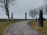 Ein gepflasterter Weg führt entlang von einzelnen Skulpturen. Die Skulpturen stehen auf grünen Wiesen.