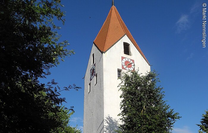 Großer Kirchturm umrahmt von hohen Bäumen.