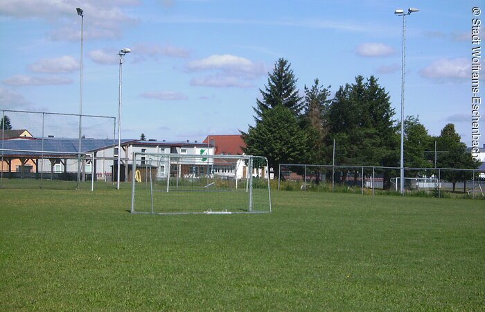 Sportplatz in Wolframs-Eschenbach Blick auf eine Hälfte eines Sportplatzes mit Fußballtor. Im Hintergrund sind links ein Sportheim und rechts eine Baumreihe zu erkennen.