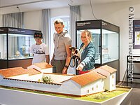 Eine Familie besucht die Abteilung der Abteilung Vor- und Frühgeschichte im Museum. Sie Blicken auf eine Nachbildung einer sogenannten Villa Rustica.