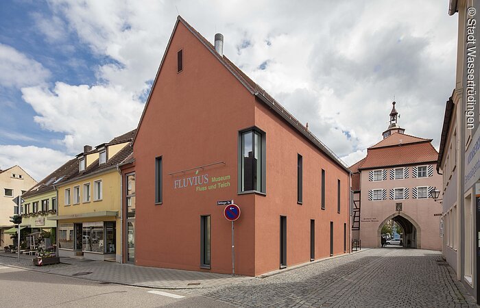 Museum Fluvius Wassertrüdingen Außenansicht eines Gebäudes mit orangener Fassade. Links und hinter dem Haus weitere Häuser einer Altstadt.