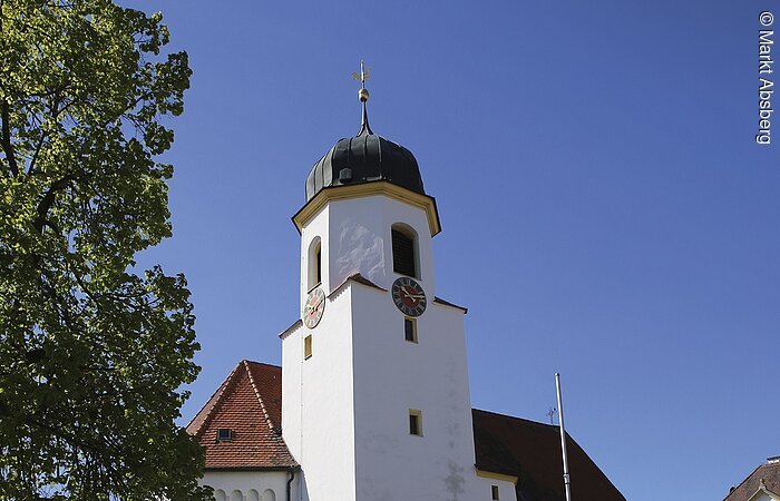 Eine weiße Kirche mit Kirchturm. Davor ein gepflasterter Hof.