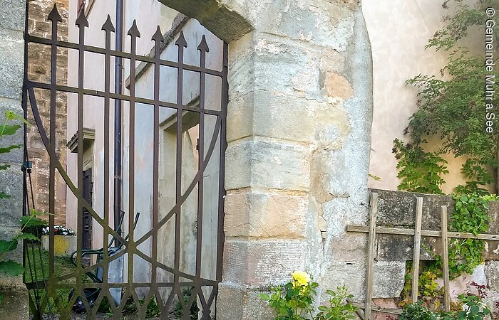 Schloss Altenmuhr - Tor Ein Tor aus Metall in einem Gemauerten Steinbogen. An die Mauer schließt ein Haus an.