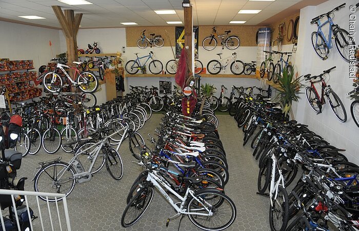 Blick auf den Verkaufsraum eines Fahrradhändlers. Viele Fahrräder stehen in drei Reihen im Raum. Auch an der weißen Wand hängen Fahrräder.