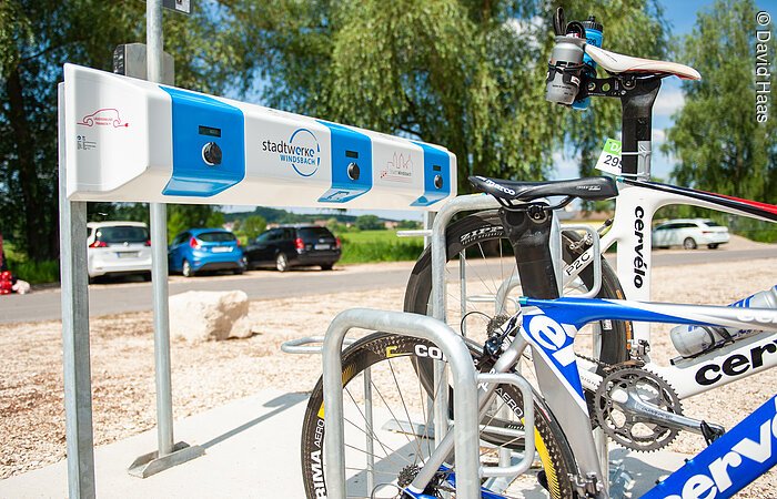 E-Bike Ladestation der Stadtwerke Windsbach Eine Ladestation für Elektro-Fahrräder. Ein blau-weißer Ladebalken. Davor stehen zwei Rennräder.