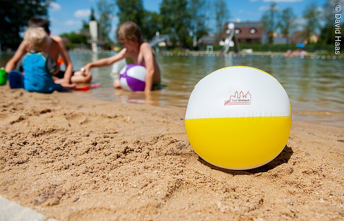 Sandstrand Im Vordergrund ein Wasserball am Strand. Dahinter spielen Kinder am Strandufer.
