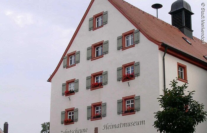 Ein Haus im fränkischen Baustil mit vier Stöcken An der Hausfront in jedem Geschoss Fenster mit grünen Fensterläden. Auf der Fassade ist zu lesen: Merkendorfer Heimatmuseum