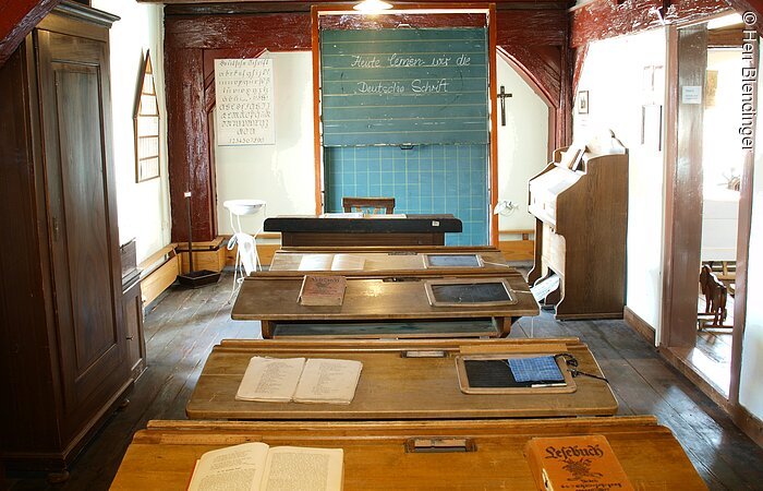 Ein alter Schulraum im Heimatmueseum Merkendorf. Ein Raum in welchem vier alte Schulbänke aus Holz hintereinander in einer Reihe stehen. Ganz vorne eine grüne Kreidetafel.