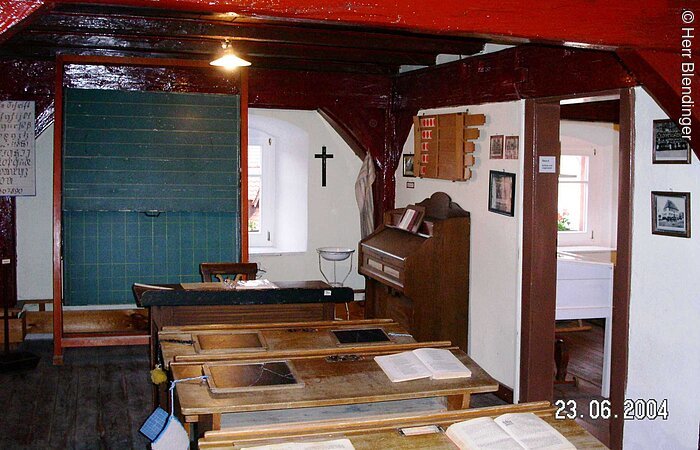 Ein alter Schulraum im Heimatmueseum Merkendorf. Ein Raum in welchem vier alte Schulbänke aus Holz hintereinander in einer Reihe stehen. Ganz vorne eine grüne Kreidetafel.