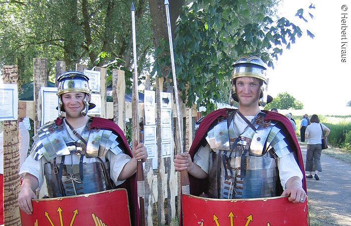 Zwei Männer verkleidet als römische Legionäre. Sie trage eine metallenen Brustpanzer und Helm. Eine Lanze und ein rotes Schutzschild.